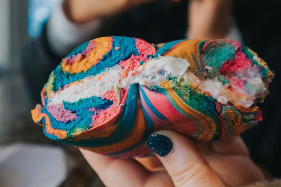 A rainbow bagel cut in half with cream cheese being held in a woman's hand